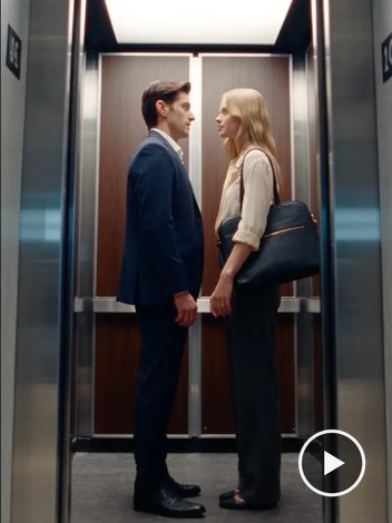 A man and woman in work clothes facing each other inside an office elevator.